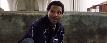 Movie still from “All About the Benjamins” (2002), directed by Kevin Bray – A man in a black and white jacket sitting on a wall; Close Up shot, Over the shoulder angle