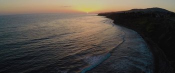 Movie still from “All Eyez on Me” (2017), directed by Benny Boom – The sun is setting over the ocean with waves in the foreground; Extreme Wide shot, High angle