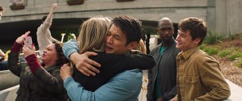 Movie still from “All My Life” (2020), directed by Marc Meyers – A man and a woman hugging each other in front of a group of people; Medium shot, Over the shoulder angle