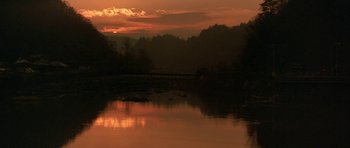 Movie still from “All the Real Girls” (2003), directed by David Gordon Green – A body of water with a bridge in the middle of it at sunset; Extreme Wide shot, High angle