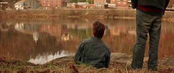 Movie still from “All the Real Girls” (2003), directed by David Gordon Green – A man sitting on the ground near a body of water; Wide shot, High angle