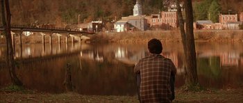 Movie still from “All the Real Girls” (2003), directed by David Gordon Green – A man looking out over a river at a town; Wide shot, High angle