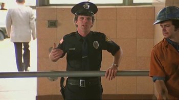 Movie still from “Alligator” (1980), directed by Lewis Teague – A police officer in uniform standing in front of a railing; Medium shot, Low angle