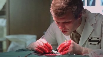 Movie still from “Alligator” (1980), directed by Lewis Teague – A man in a suit and tie cutting something with a knife; Close Up shot, Low angle