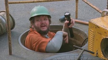 Movie still from “Alligator” (1980), directed by Lewis Teague – A man with a hard hat is in a manhole with a flashlight; Medium shot, High angle