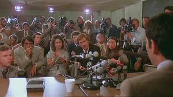 Movie still from “Alligator” (1980), directed by Lewis Teague – A group of people sitting around a table with microphones; Wide shot, Over the shoulder angle
