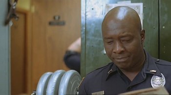 Movie still from “Alligator” (1980), directed by Lewis Teague – A man in a police uniform sitting in front of a pair of dumbbells; Close Up shot, Low angle