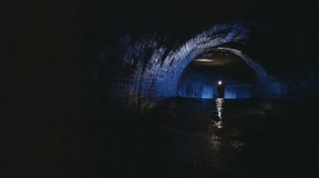 Movie still from “Alligator” (1980), directed by Lewis Teague – A person standing in a dark tunnel with a light on; Extreme Wide shot, High angle