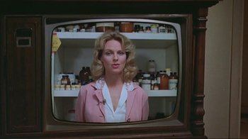 Movie still from “Alligator” (1980), directed by Lewis Teague – A woman in a pink jacket standing in front of a television; Close Up shot, Low angle