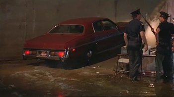 Movie still from “Alligator” (1980), directed by Lewis Teague – A man standing next to an old car in a parking lot; Wide shot, High angle
