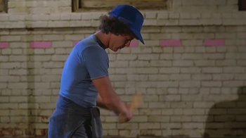 Movie still from “Alligator” (1980), directed by Lewis Teague – A man in a blue hat is playing with a wooden stick; Medium shot, Low angle