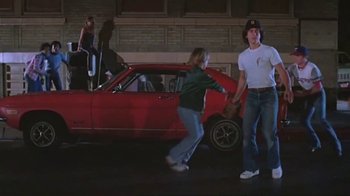 Movie still from “Alligator” (1980), directed by Lewis Teague – A couple of people standing next to a red car; Wide shot, Low angle