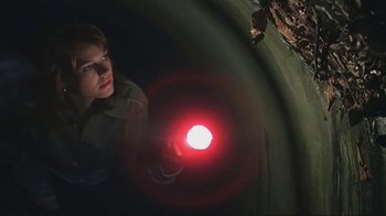 Movie still from “Alligator” (1980), directed by Lewis Teague – A person with a red light in a dark room; Medium shot, Overhead angle
