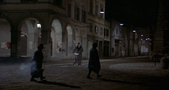 Movie still from “Amarcord” (1973), directed by Federico Fellini – A group of people walking down a street at night; Extreme Wide shot, High angle