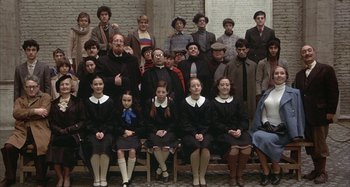 Movie still from “Amarcord” (1973), directed by Federico Fellini – A group of people sitting on a bench in front of a brick wall; Wide shot, High angle