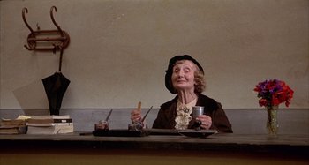 Movie still from “Amarcord” (1973), directed by Federico Fellini – An older woman sitting at a table with a cup of coffee; Medium shot, Low angle