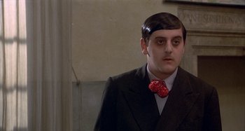 Movie still from “Amarcord” (1973), directed by Federico Fellini – A man in a black suit and a red bow tie; Close Up shot, Over the shoulder angle