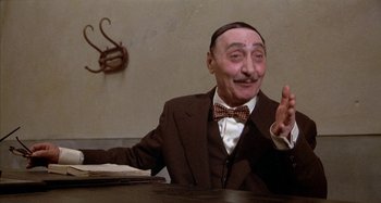 Movie still from “Amarcord” (1973), directed by Federico Fellini – An older man sitting at a table in front of a wall; Medium shot, High angle