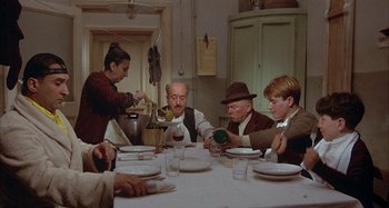 Movie still from “Amarcord” (1973), directed by Federico Fellini – A group of people sitting around a table with plates; Wide shot, High angle
