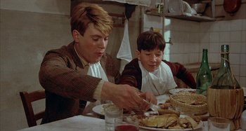 Movie still from “Amarcord” (1973), directed by Federico Fellini – A man and a boy sitting at a table with food; Medium shot, Low angle