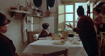 Movie still from “Amarcord” (1973), directed by Federico Fellini – Two people sitting at a table in a kitchen; Medium shot, Over the shoulder angle