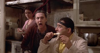 Movie still from “Amarcord” (1973), directed by Federico Fellini – A group of people sitting in a room eating food; Medium shot, High angle