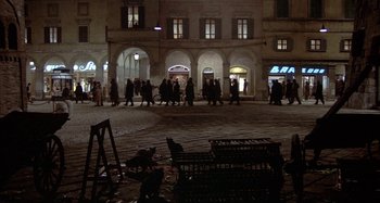 Movie still from “Amarcord” (1973), directed by Federico Fellini – A group of people walking in a courtyard at night; Extreme Wide shot, High angle
