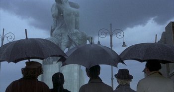 Movie still from “Amarcord” (1973), directed by Federico Fellini – A group of people standing under umbrellas in the rain; Wide shot, High angle