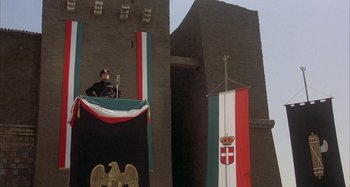 Movie still from “Amarcord” (1973), directed by Federico Fellini – A man standing in front of a microphone on top of a stage; Wide shot, Low angle