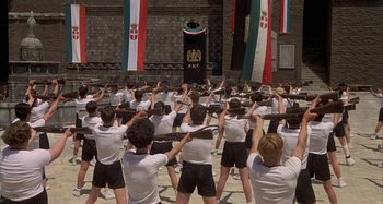 Movie still from “Amarcord” (1973), directed by Federico Fellini – A large group of young men standing in front of a building; Wide shot, High angle