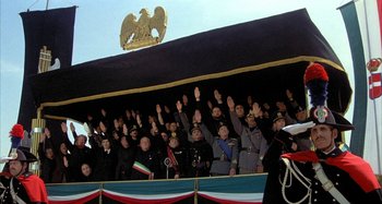 Movie still from “Amarcord” (1973), directed by Federico Fellini – A group of people in military uniforms raising their hands; Wide shot, Low angle