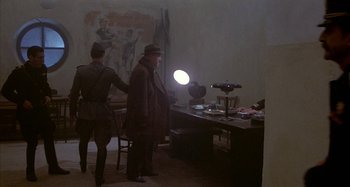 Movie still from “Amarcord” (1973), directed by Federico Fellini – A man in a hat standing in front of a desk; Wide shot, High angle