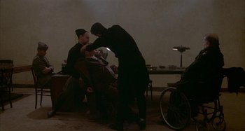 Movie still from “Amarcord” (1973), directed by Federico Fellini – A man in a black suit is shaving another man's beard; Wide shot, Over the shoulder angle
