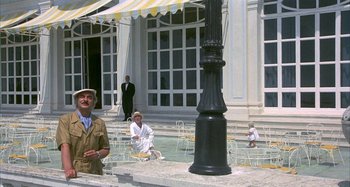Movie still from “Amarcord” (1973), directed by Federico Fellini – A man in a brown suit standing in front of a pool; Wide shot, Low angle