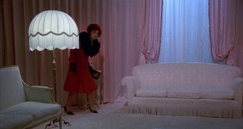 Movie still from “Amarcord” (1973), directed by Federico Fellini – A woman in a red dress holding a white umbrella in front of a couch; Wide shot, High angle