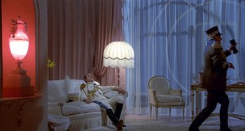 Movie still from “Amarcord” (1973), directed by Federico Fellini – A man sitting on a chair next to a lamp in a living room; Wide shot, High angle