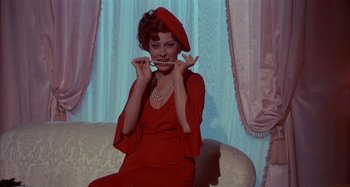 Movie still from “Amarcord” (1973), directed by Federico Fellini – A woman in a red dress and a red hat is sitting on a couch; Medium shot, Over the shoulder angle