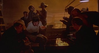 Movie still from “Amarcord” (1973), directed by Federico Fellini – A group of people sitting around a fire pit; Wide shot, High angle