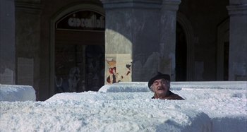 Movie still from “Amarcord” (1973), directed by Federico Fellini – An old man in a hat is sitting in a pile of snow; Wide shot, High angle
