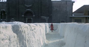 Movie still from “Amarcord” (1973), directed by Federico Fellini – A person in a red coat is walking through snow; Extreme Wide shot, High angle