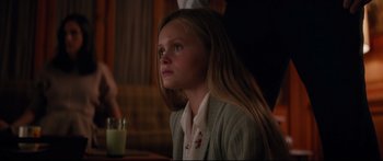 Movie still from “American Pastoral” (2016), directed by Ewan McGregor – A young girl sitting at a table with a glass; Medium shot, Over the shoulder angle