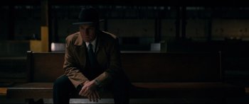 Movie still from “American Pastoral” (2016), directed by Ewan McGregor – A man sitting on a bench wearing a suit and a hat; Medium shot, Low angle