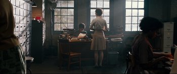 Movie still from “American Pastoral” (2016), directed by Ewan McGregor – A woman standing in front of a man at a desk; Wide shot, High angle