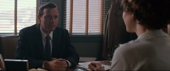 Movie still from “American Pastoral” (2016), directed by Ewan McGregor – A man in a suit sitting at a table with another man; Medium shot, Over the shoulder angle