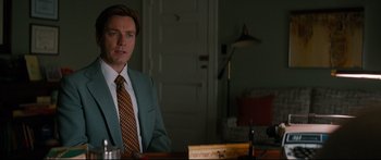 Movie still from “American Pastoral” (2016), directed by Ewan McGregor – A man wearing a suit and tie sitting at a table; Medium shot, Over the shoulder angle