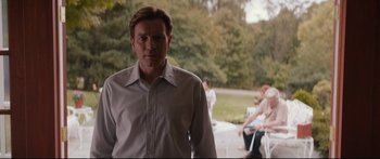 Movie still from “American Pastoral” (2016), directed by Ewan McGregor – A man standing in front of a group of people in a park; Medium shot, Over the shoulder angle