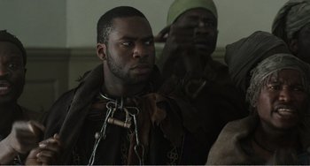 Movie still from “Amistad” (1997), directed by Steven Spielberg – A man with chains around his neck looks at the camera; Close Up shot, Over the shoulder angle