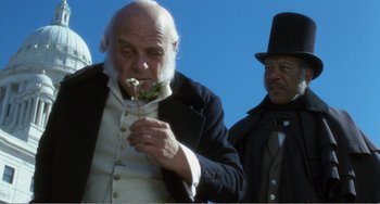 Movie still from “Amistad” (1997), directed by Steven Spielberg – A man holding a flower in front of another man; Close Up shot, Low angle