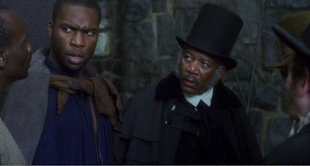 Movie still from “Amistad” (1997), directed by Steven Spielberg – A man in a top hat standing next to another man; Medium shot, Over the shoulder angle