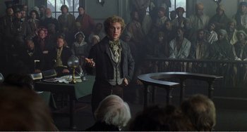 Movie still from “Amistad” (1997), directed by Steven Spielberg – A man standing in front of a crowd of people in a room; Medium shot, Low angle